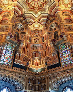 Elaborate gold-decorated Gothic ceiling with ornate arches, patterns, and stained glass windows in historic castle interior