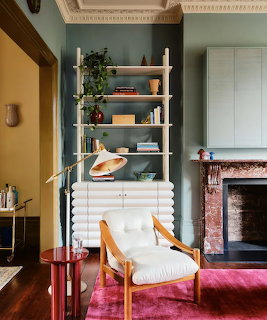 White fluted shelving cabinet behind an armchair in a cozy room with a pink rug and fireplace