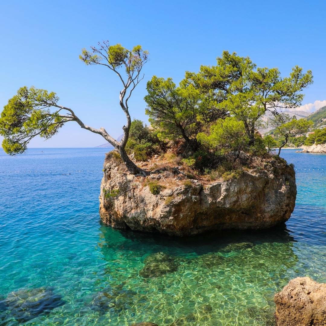 Small rocky island with green trees in turquoise sea water under blue sky