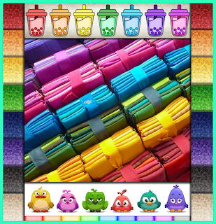 Rainbow-colored fabric rolls tied with ribbons, arranged diagonally in rows from pink to purple to blue to yellow to red