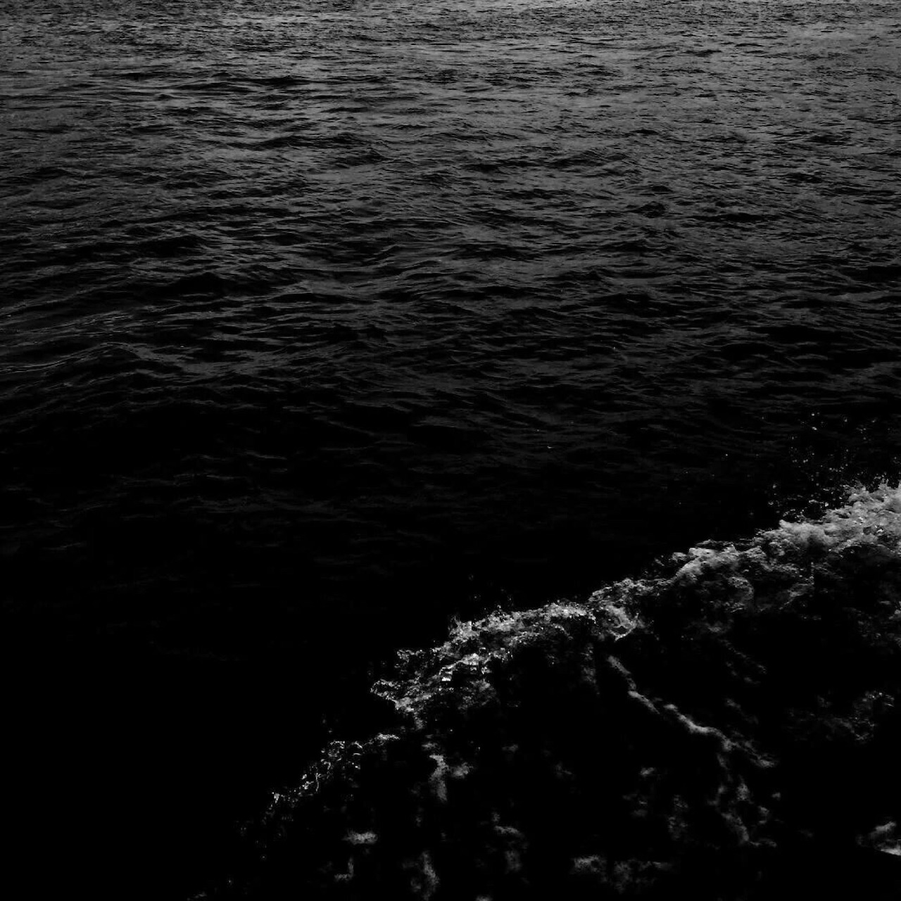 Black and white ocean surface with a foamy wave in the lower right