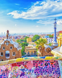 Colorful mosaic wall at Park Güell overlooking Barcelona cityscape with Gaudí buildings and blue sky