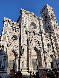 Ornate white and green marble facade of Florence Cathedral with bell tower against blue sky