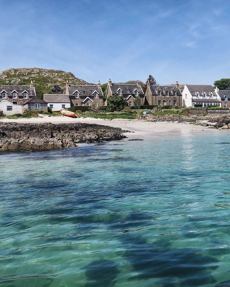 Traditional stone houses beside a turquoise bay with beach and rocky shore under blue sky