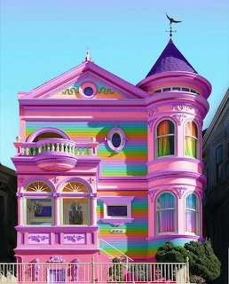 Bright pink Victorian house with rainbow stripes, bay windows, and a turret under a clear blue sky