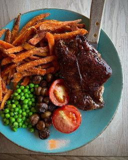 Plate of BBQ ribs with sweet potato fries, vegetables including peas, tomato, and mushrooms on turquoise plate