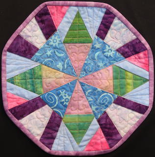 Octagonal quilted mandala with symmetrical triangular pattern in purple, pink, green and blue fabrics