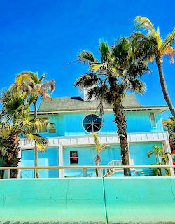 Turquoise coastal house with palm trees and blue sky