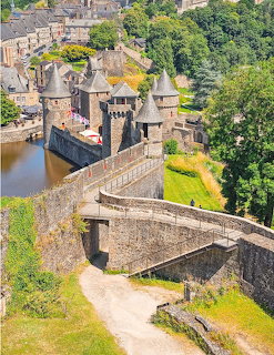 Aerial view of Chateau de Fougères with stone towers, fortified walls, moat, and village in background