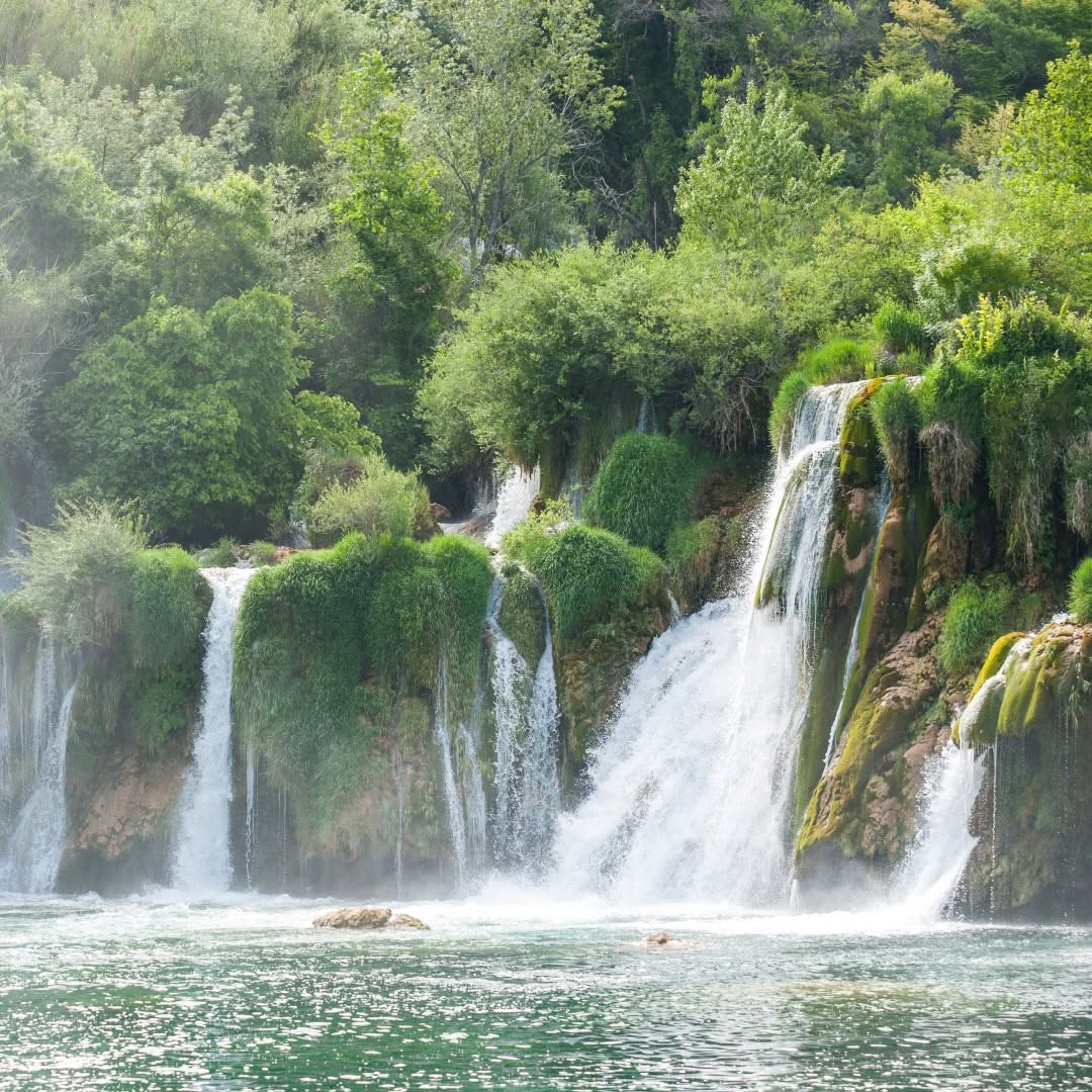 Waterfalls flowing through lush green forest into turquoise pool