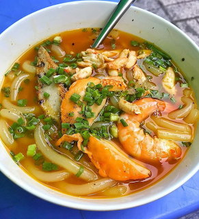 Bowl of Vietnamese crab noodle soup with thick noodles, orange broth, and green onions