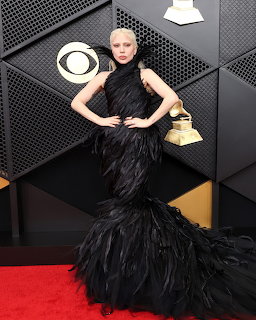 Woman in elaborate black feathered mermaid gown posing on red carpet at Grammy Awards
