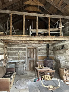 Rustic log cabin interior with loft, chairs, table, and wood stove