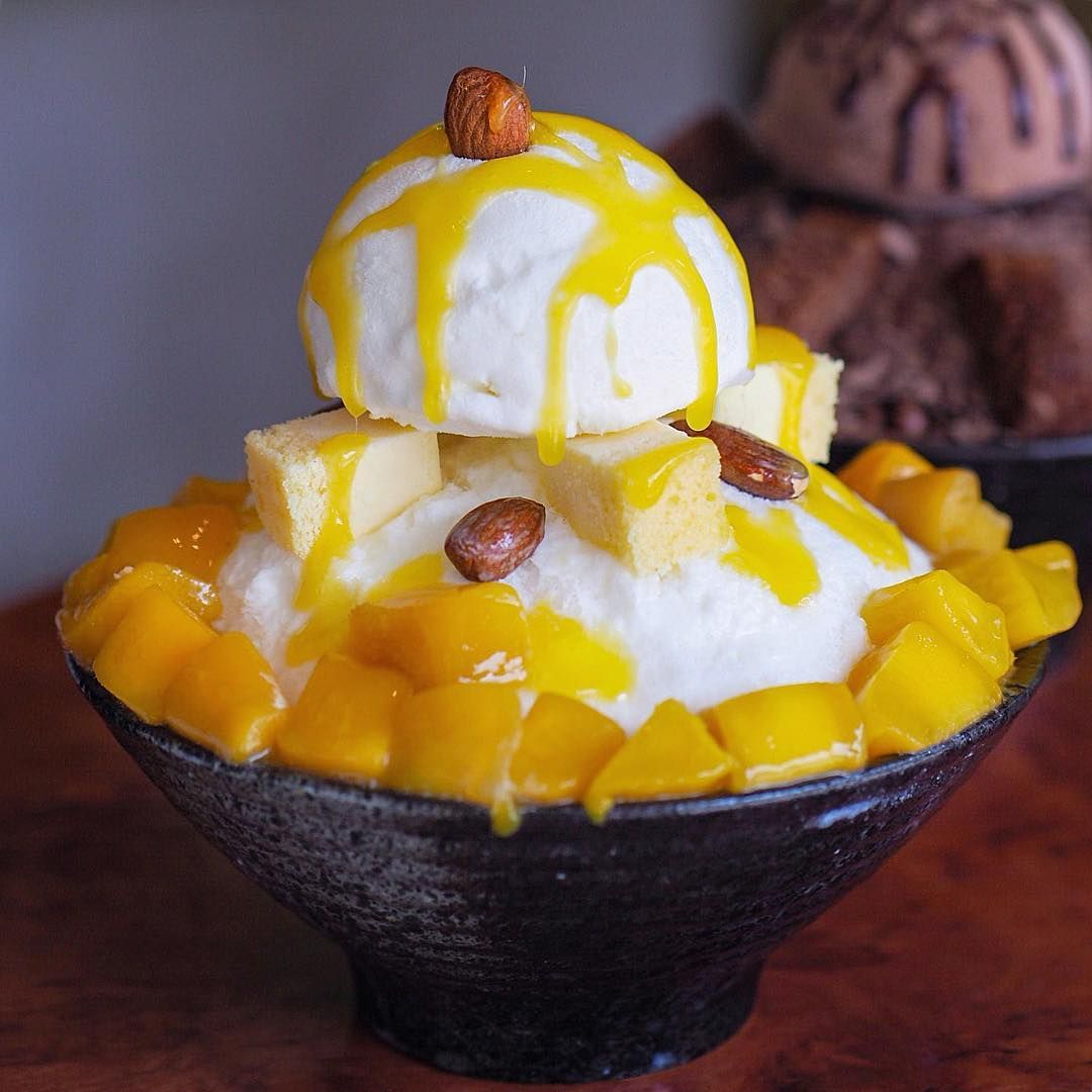Mango shaved ice in a black bowl topped with vanilla ice cream, mango cubes, and yellow syrup