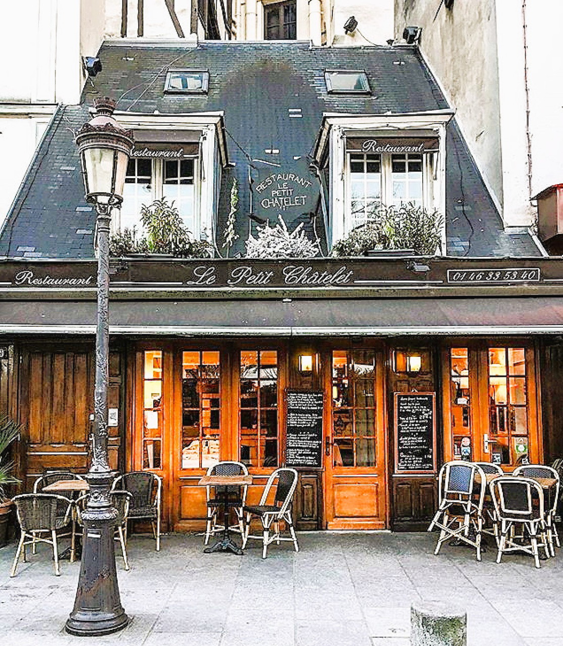French cafe storefront with orange wood facade and outdoor tables on Paris sidewalk