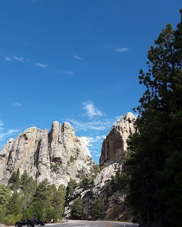 Road view approaching Mount Rushmore memorial with carved rock faces visible among trees and blue sky