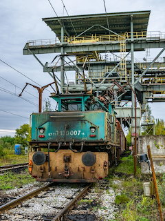 Old electric locomotive on railway tracks under an industrial maintenance gantry