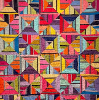 Colorful geometric patchwork quilt with triangular and square blocks in vibrant multicolored fabrics