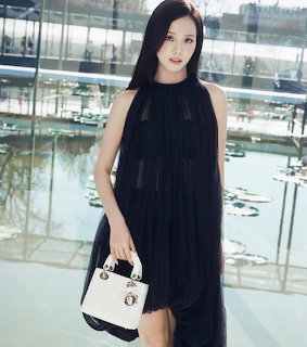 Woman in a black dress standing indoors near glass railings and reflective water
