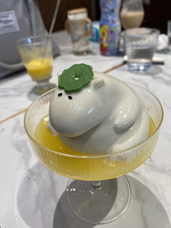 White panna cotta with green leaf in glass coupe dish with orange sauce on restaurant table
