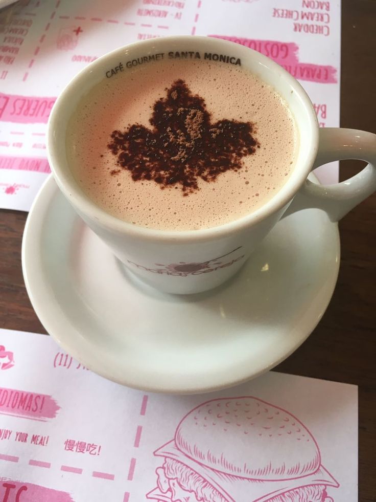 Coffee cup with leaf-shaped latte art on foam, white cup and saucer, pink menus underneath