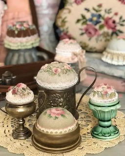Vintage pin cushions with floral embroidery and ornate metal bases arranged on lace doily