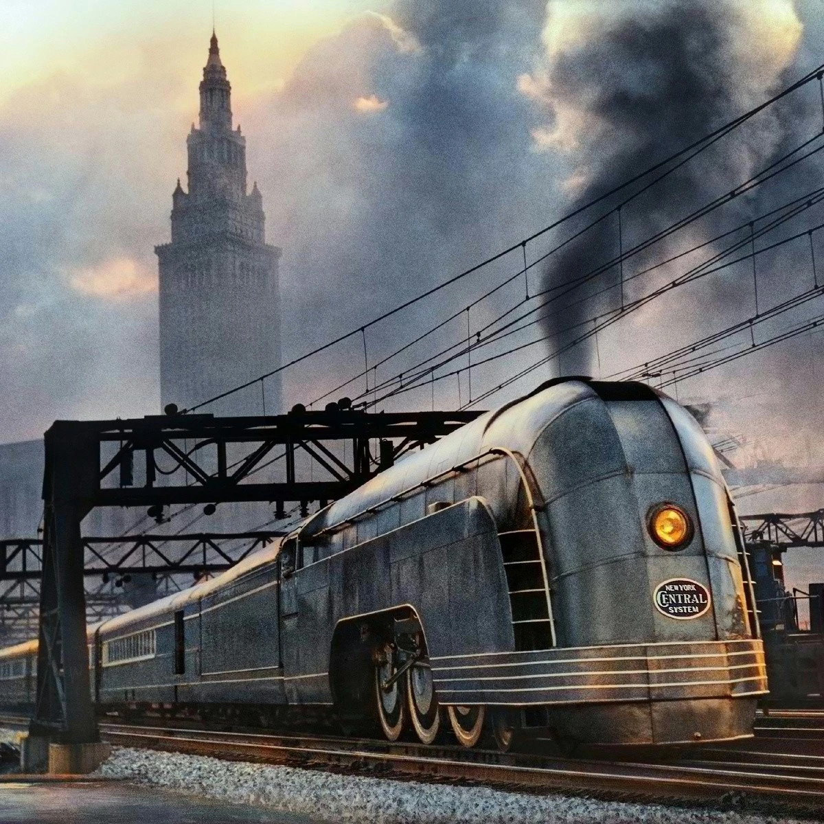Silver streamlined steam locomotive with art deco styling passing under bridge with city tower and dramatic sky