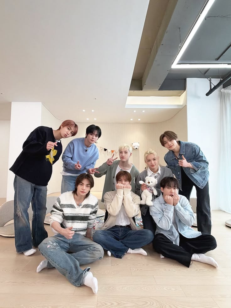 Seven young men in casual attire posing together in a bright modern studio space