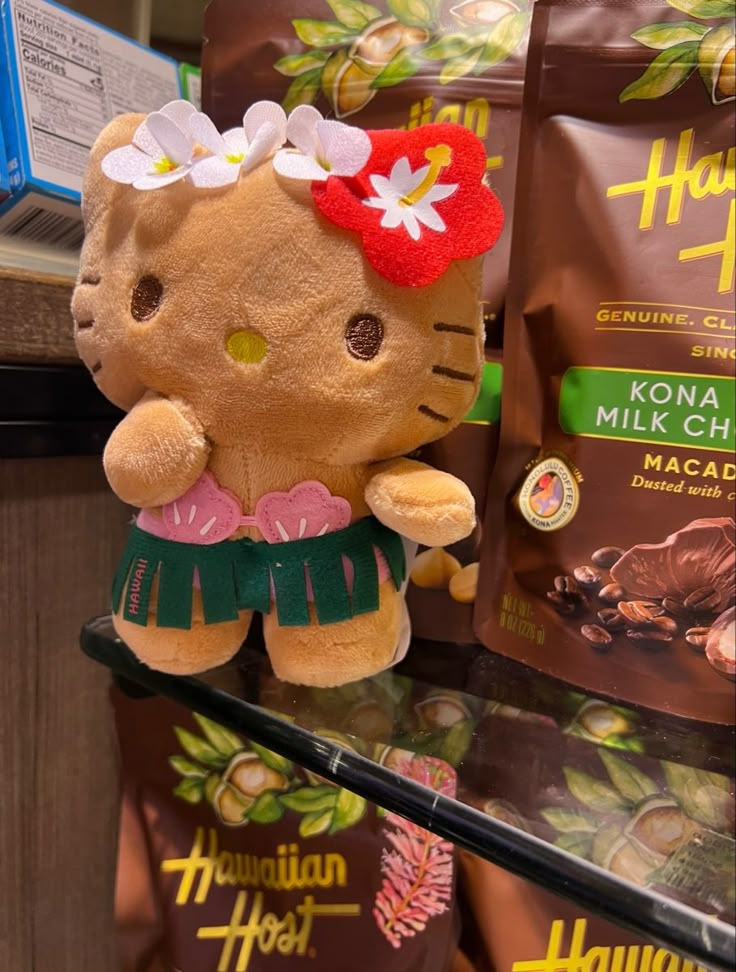 Hello Kitty plush in Hawaiian hula costume with flower headband, surrounded by Hawaiian Host chocolate bags