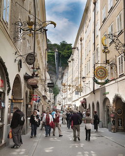 Busy pedestrian shopping street in Salzburg with ornate iron signs and historic buildings