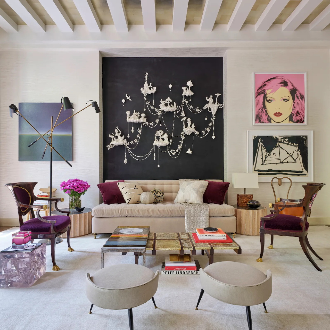 Elegant living room with beige sofa, chandelier artwork, striped ceiling, and colorful accent pieces