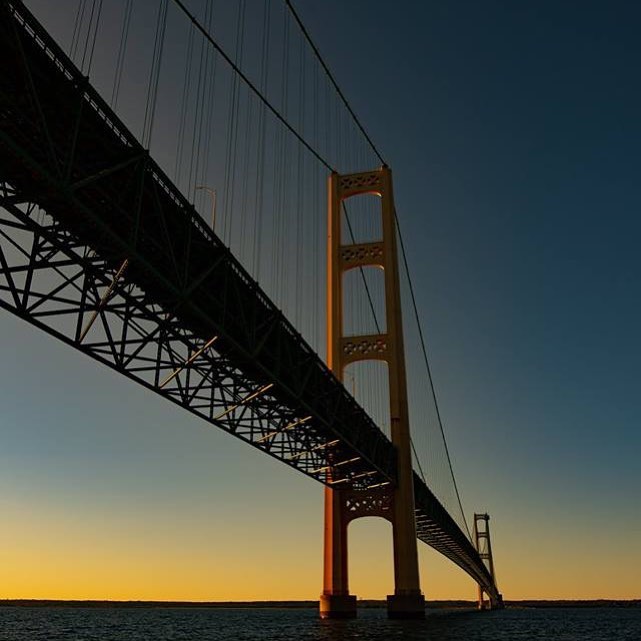 Mackinac Bridge silhouette at sunset with orange and blue gradient sky over dark water