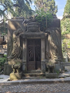 Ornate stone mausoleum with carved draped figures and decorative urn surrounded by cypress trees