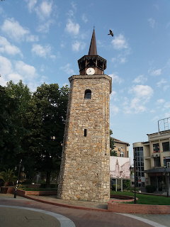 Historic stone clock tower with red pointed roof in Bulgarian city plaza