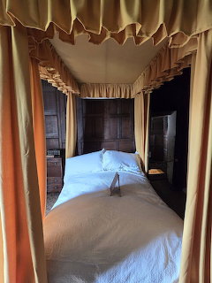 Historic four-poster bed with cream curtains and white bedding in an interior room