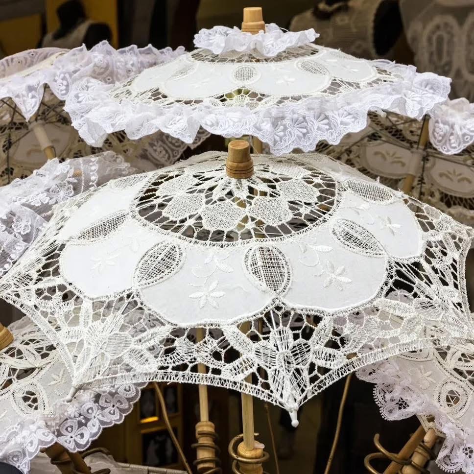 Multiple white lace parasols with ornate crochet patterns and wooden handles arranged in a decorative display