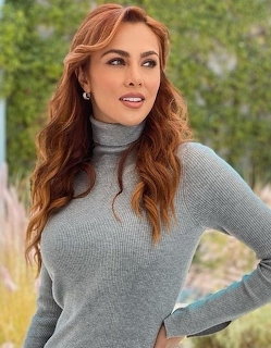 Woman with wavy auburn hair wearing gray turtleneck sweater, smiling outdoors