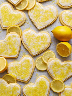 Heart-shaped lemon cookies with white icing and yellow sugar scattered among fresh lemon slices