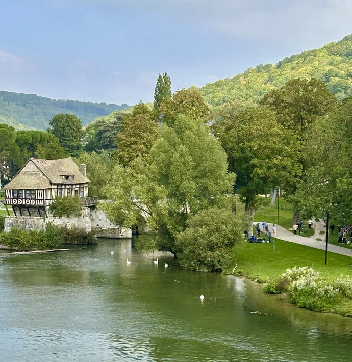 Riverside house with trees, green lawn, and hills reflected in calm water