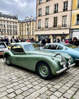 Vintage green Jaguar XK120 coupe parked on a cobblestone street in a city square