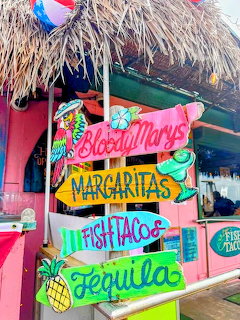 Colorful drink and food signs hanging outside a thatched tropical beach hut