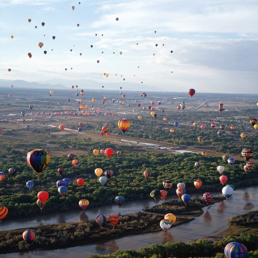 Colorful hot air balloons flying over a wide landscape with rivers and fields