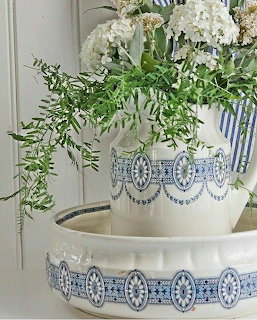 White and blue patterned ceramic vase with white hydrangeas and green ferns in a ceramic basin