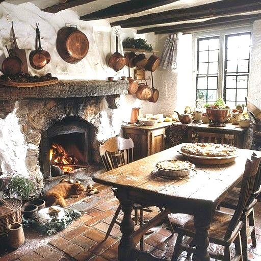 Rustic country kitchen with stone fireplace, hanging copper pots, wooden table, and a cat by the fire