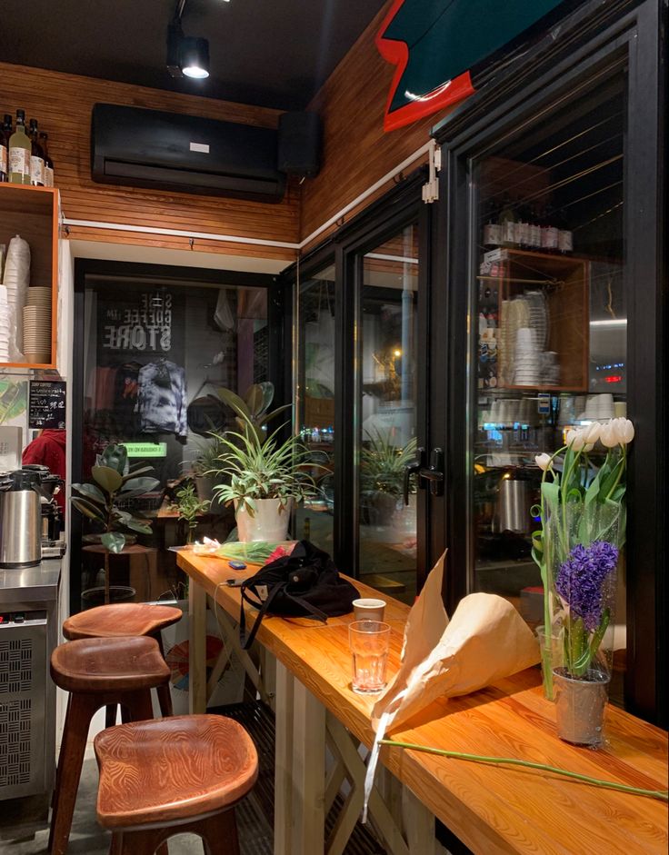 Cozy café interior with wooden counter, bar stools, potted plants, and fresh flowers