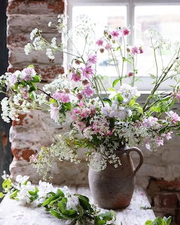 Pink and white wildflower bouquet in brown ceramic vase by window with brick wall