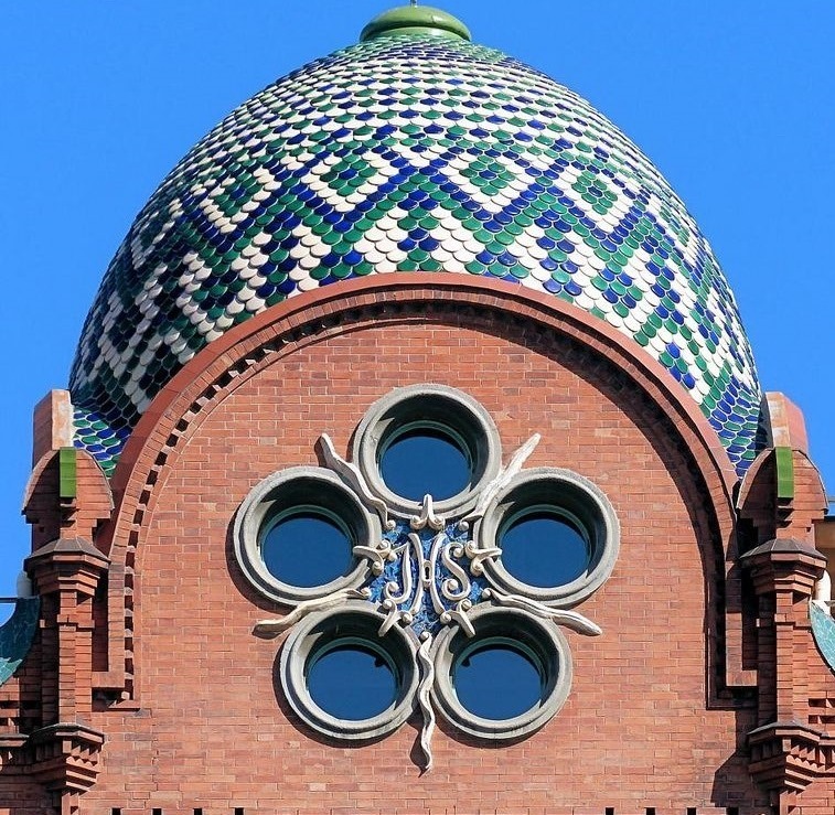 Brick building facade with circular windows and a blue-green patterned dome under a clear sky