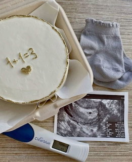 Pregnancy announcement with cake reading 1+1=3, baby socks, ultrasound image, and positive pregnancy test