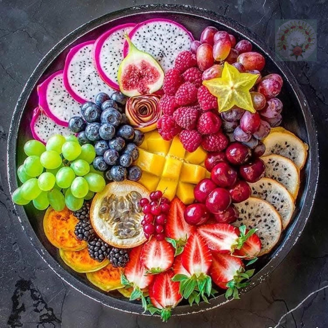 Round platter filled with colorful sliced fresh fruit on a dark background