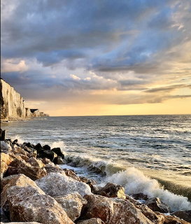 Waves crashing on rocky shore with white chalk cliffs and dramatic sunset clouds